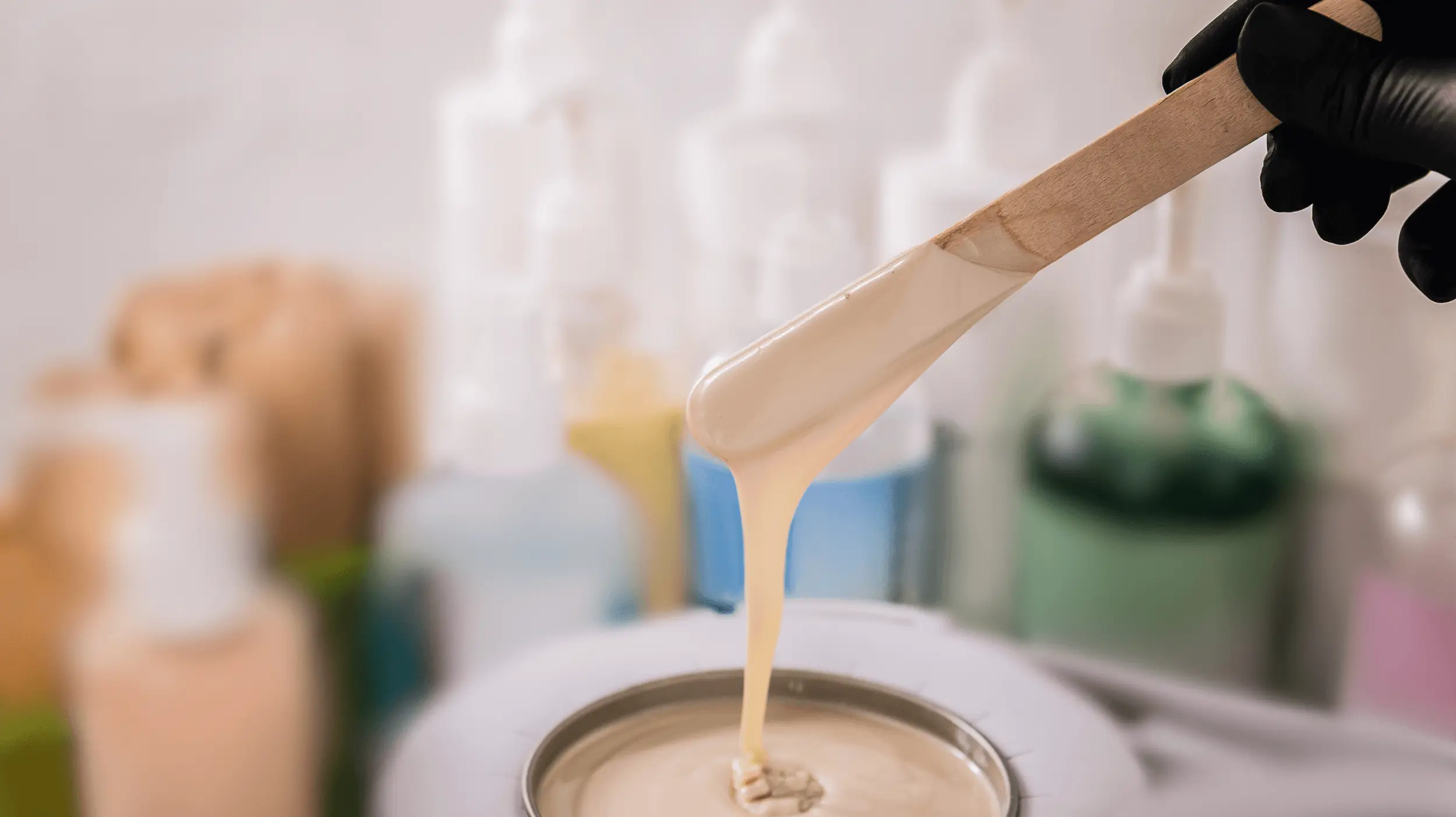 Gros plan sur une spatule en bois tenant de la cire tiède crémeuse, prête à être utilisée pour une épilation professionnelle.