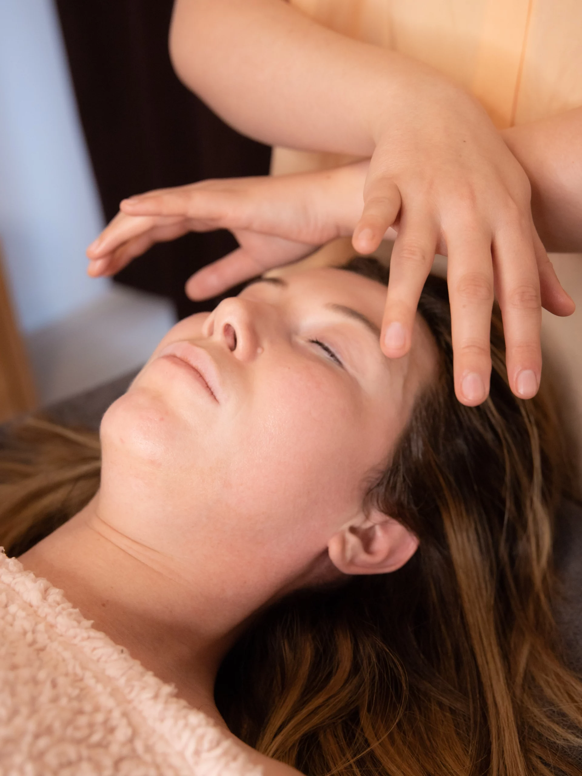 Cliente détendue allongée sur la table de soin, praticienne effectuant un massage du visage.