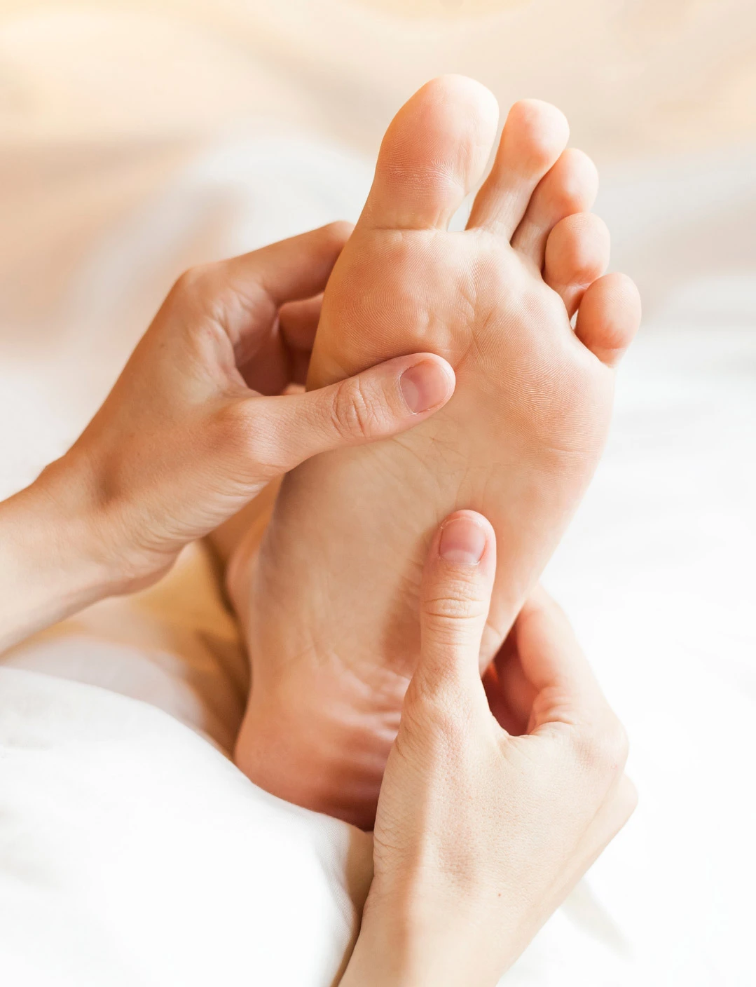 Mains d’une praticienne exerçant une pression sur la plante du pied d’une cliente lors d’une séance de réflexologie plantaire.