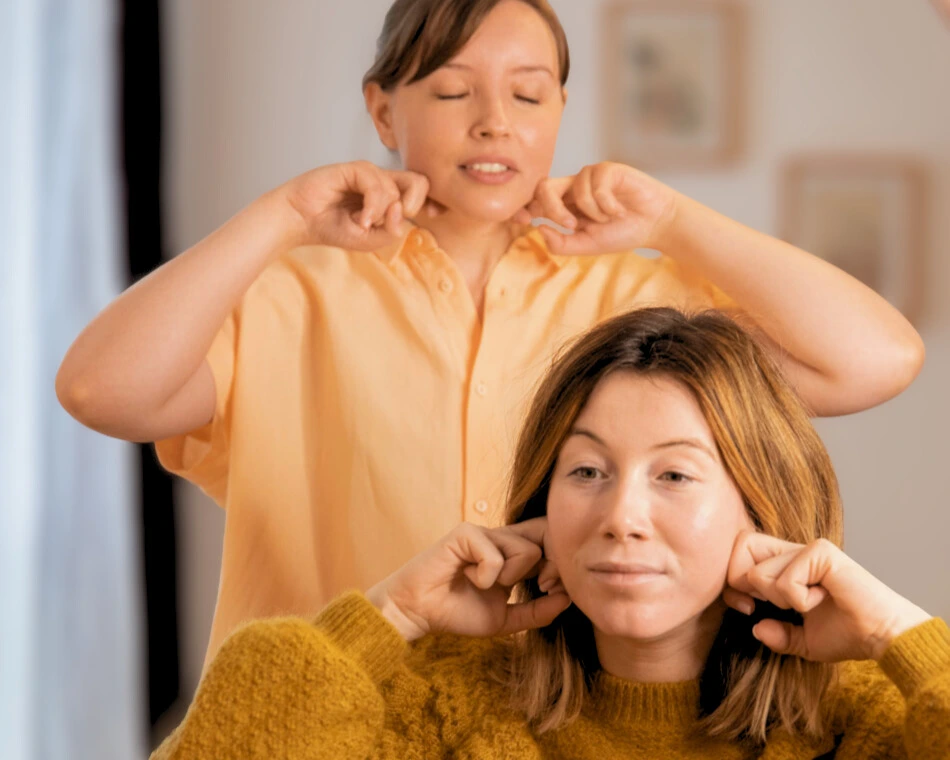 Séance d’auto-massage du visage guidée : une praticienne montre les gestes à une participante devant un miroir.